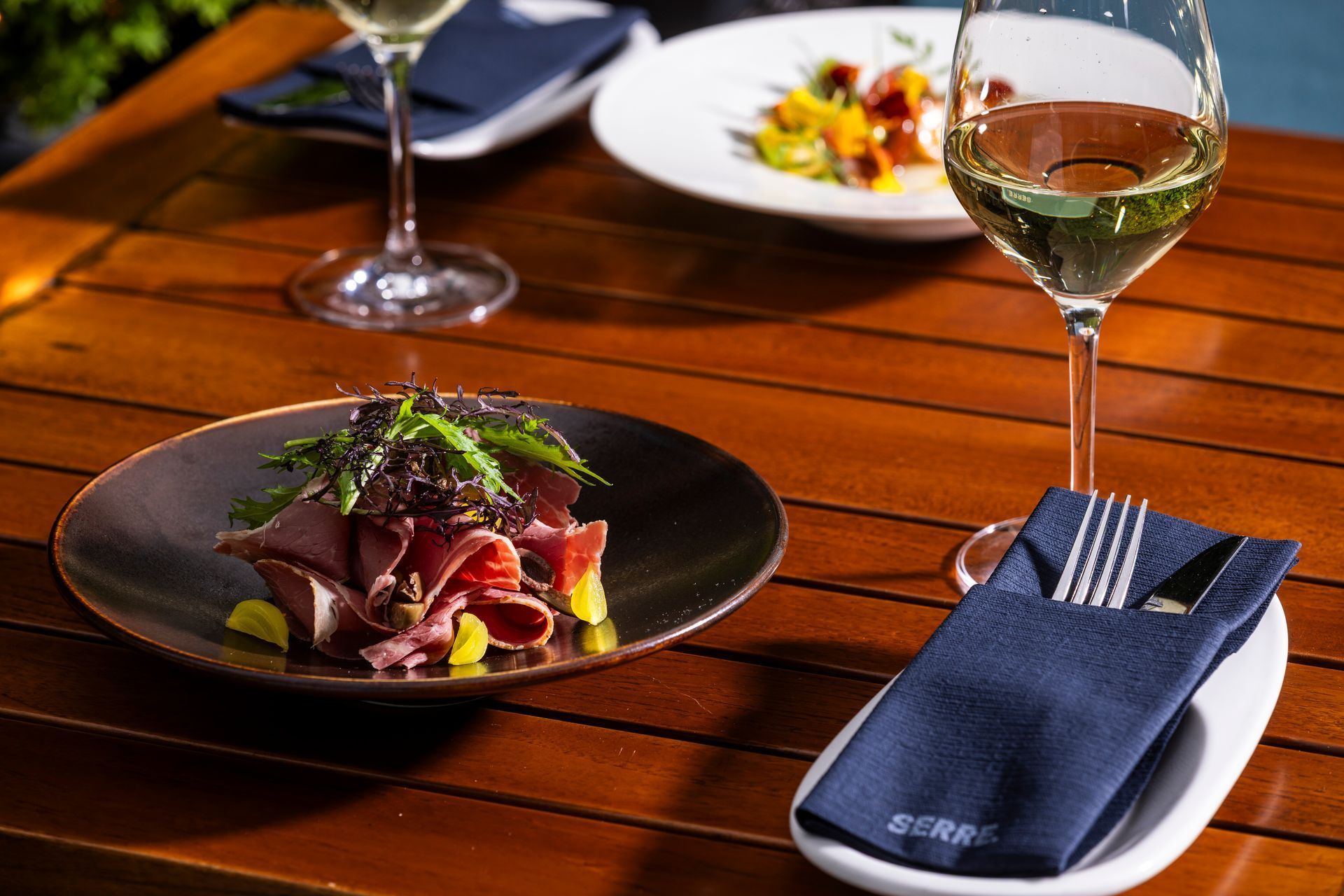 Gourmet food on wooden table with wine glasses, blue napkins, and plates.