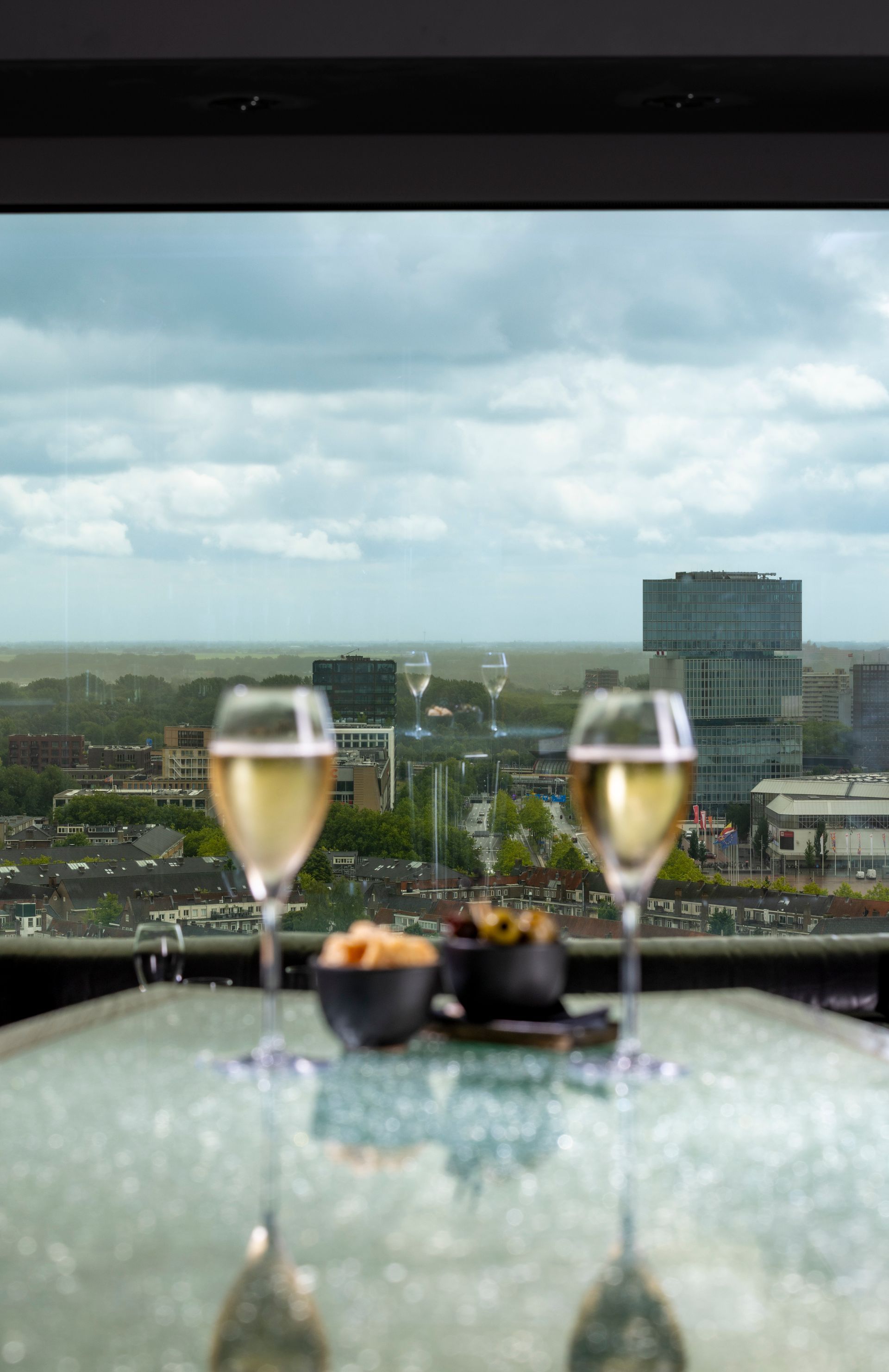 Two glasses of champagne on a table with snacks, overlooking a city skyline.