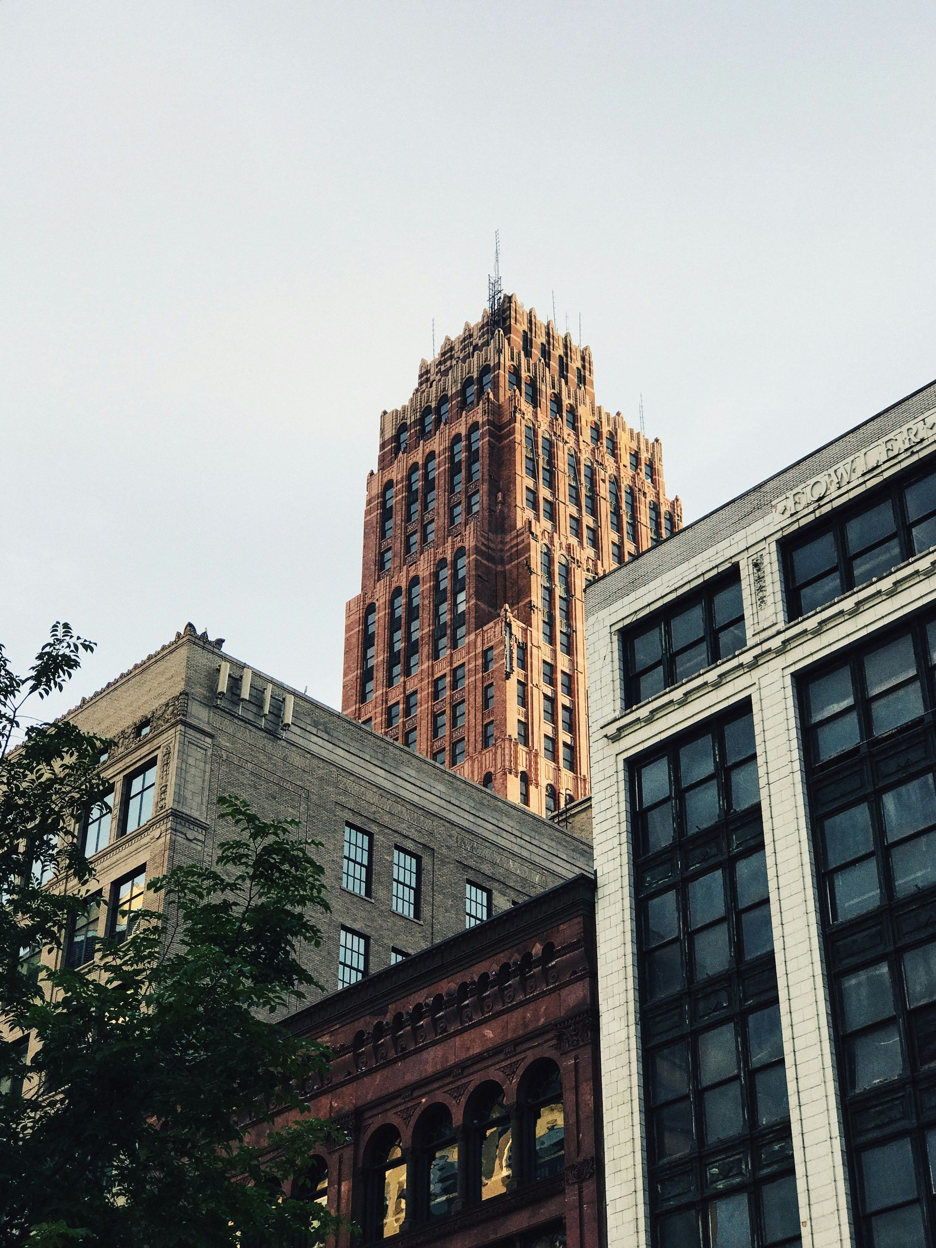 Buildings of different architectural styles under a cloudy sky; a tall, ornate brown tower dominates the view.