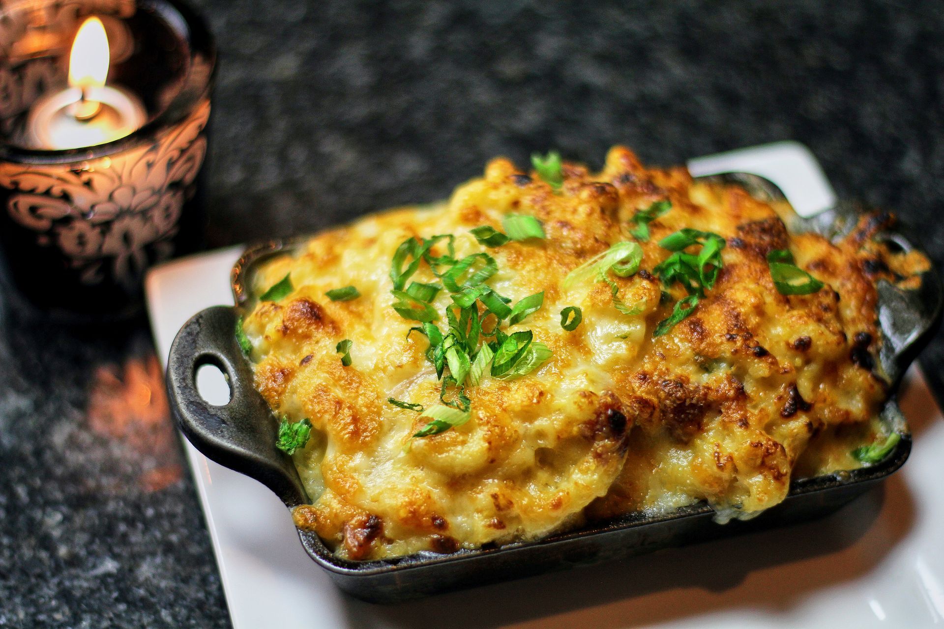 A bowl of macaroni and cheese is on a white plate next to a candle.