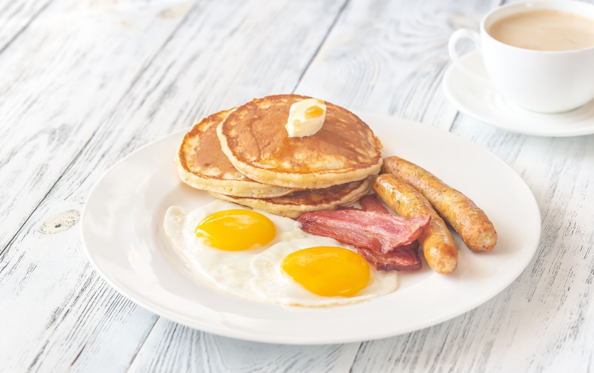 A white plate topped with pancakes , eggs , bacon and sausage.