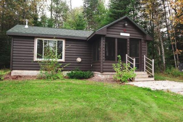 A small log cabin is sitting in the middle of a lush green field.