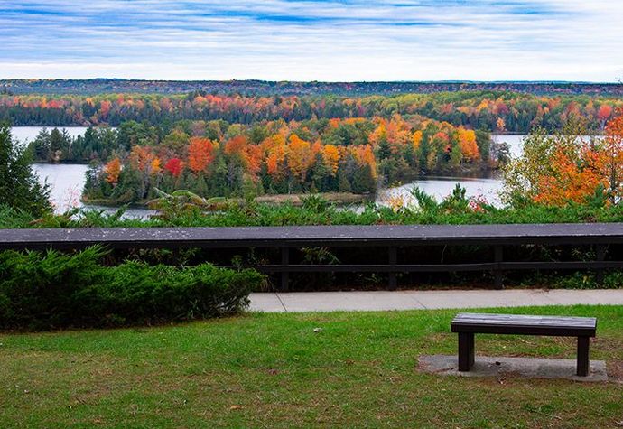 There is a bench in the foreground and a view of a lake in the background.