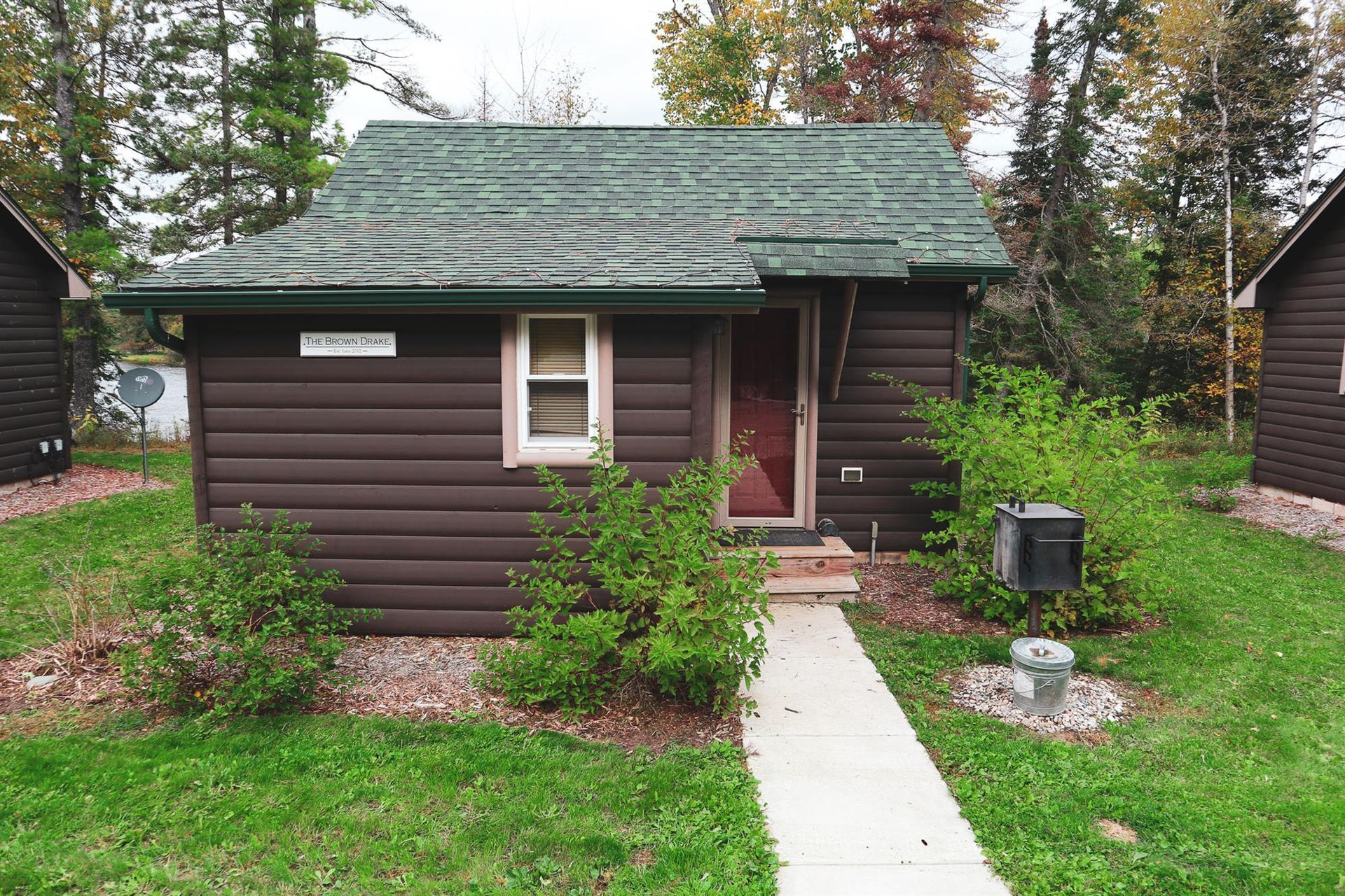 A small log cabin with a green roof and a walkway leading to it.