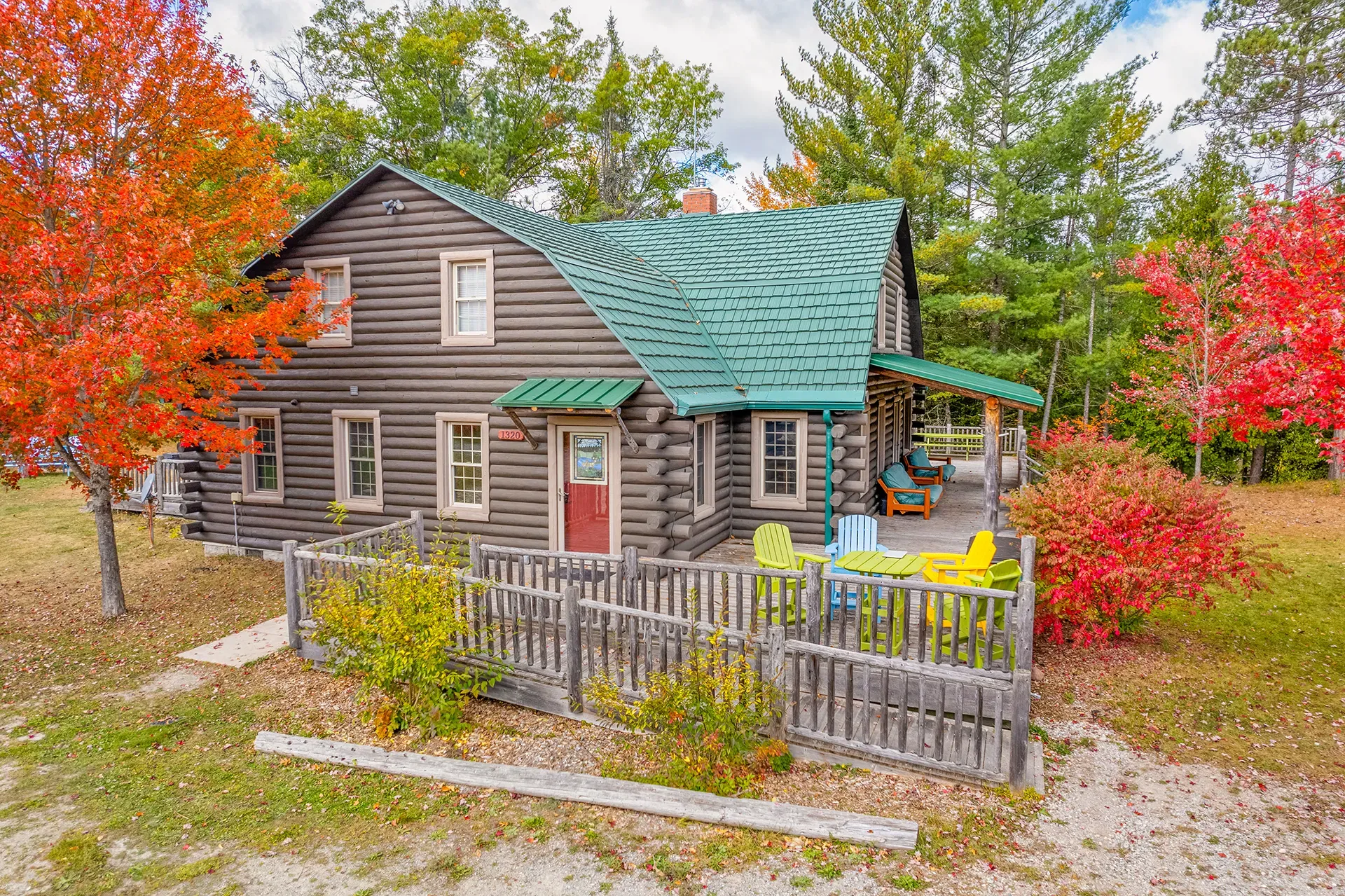 A log cabin with a green roof is surrounded by trees in the woods.