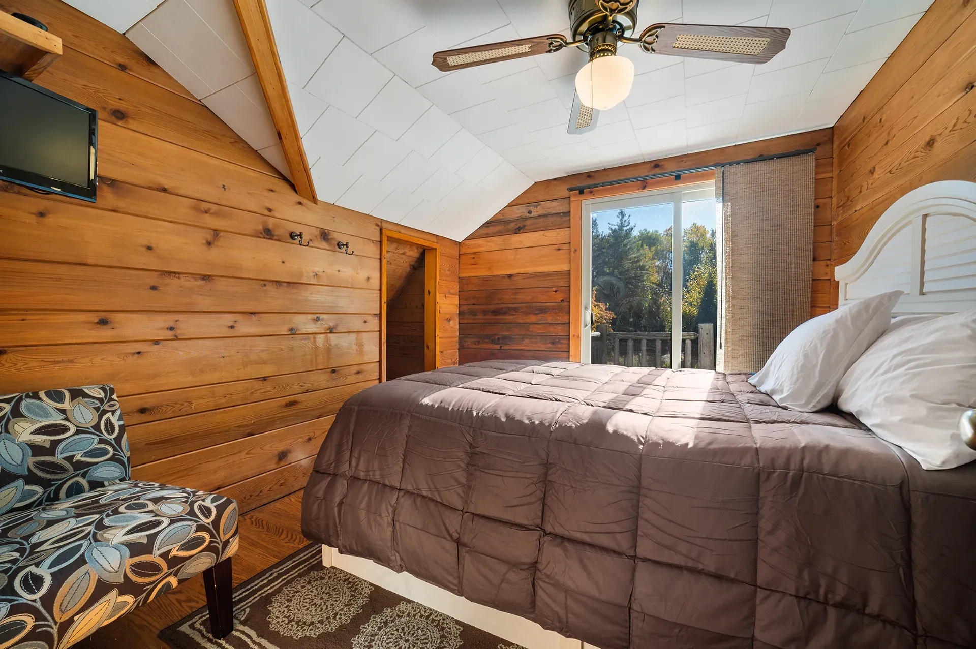 A bedroom with a bed , chair , television and ceiling fan.