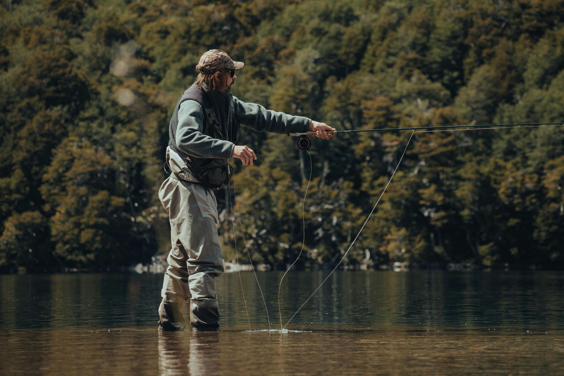 A man is fishing in a lake with trees in the background.