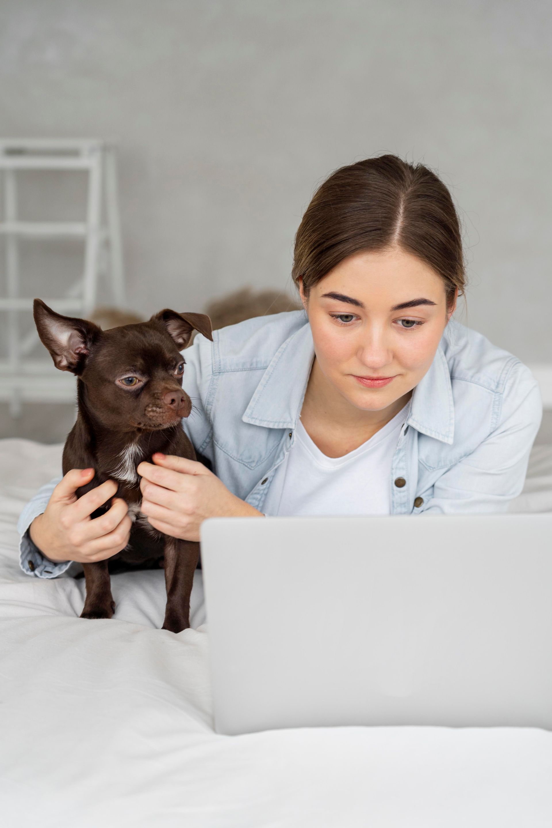 A woman is holding a small dog while looking at a laptop.