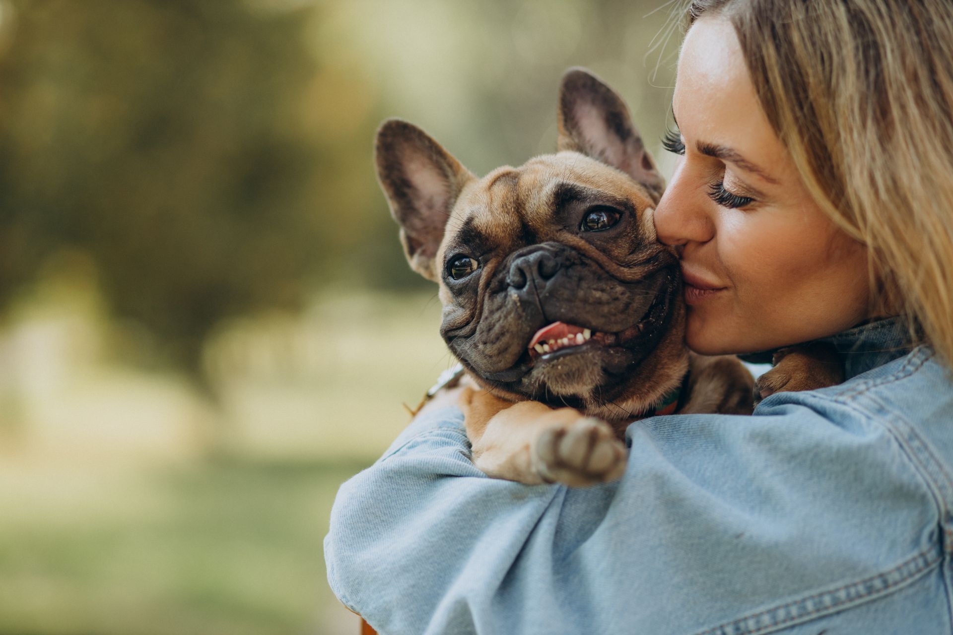 A woman is holding a french bulldog in her arms and kissing it on the nose.