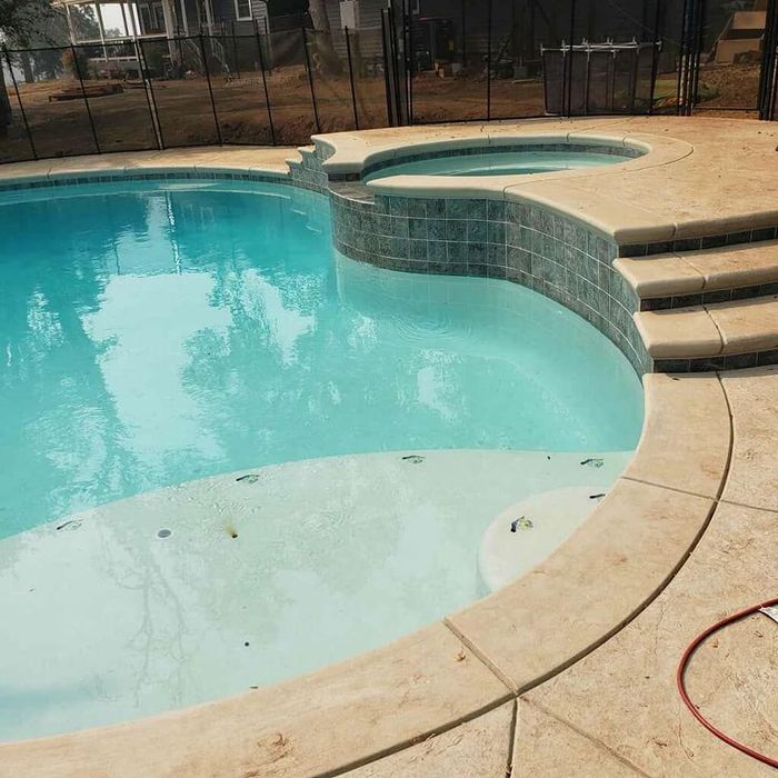 A backyard features a blue swimming pool with a partially covered top, a stone deck, lounge chairs, and a gazebo.