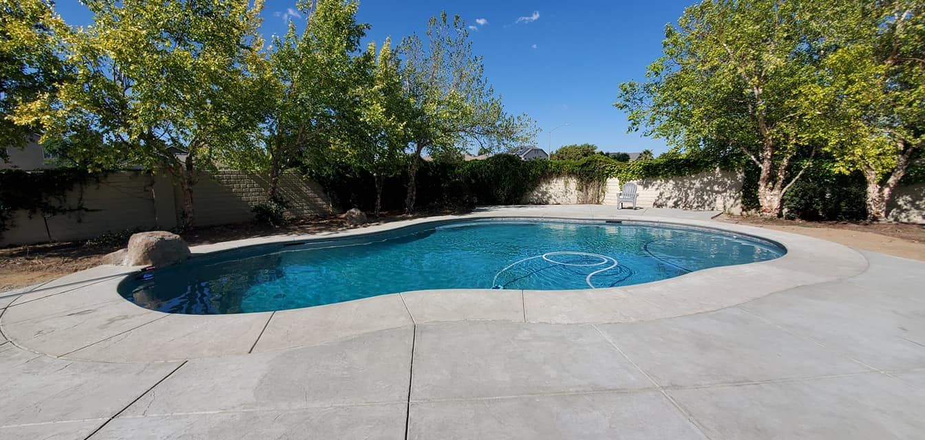 A backyard features a blue swimming pool with a partially covered top, a stone deck, lounge chairs, and a gazebo.