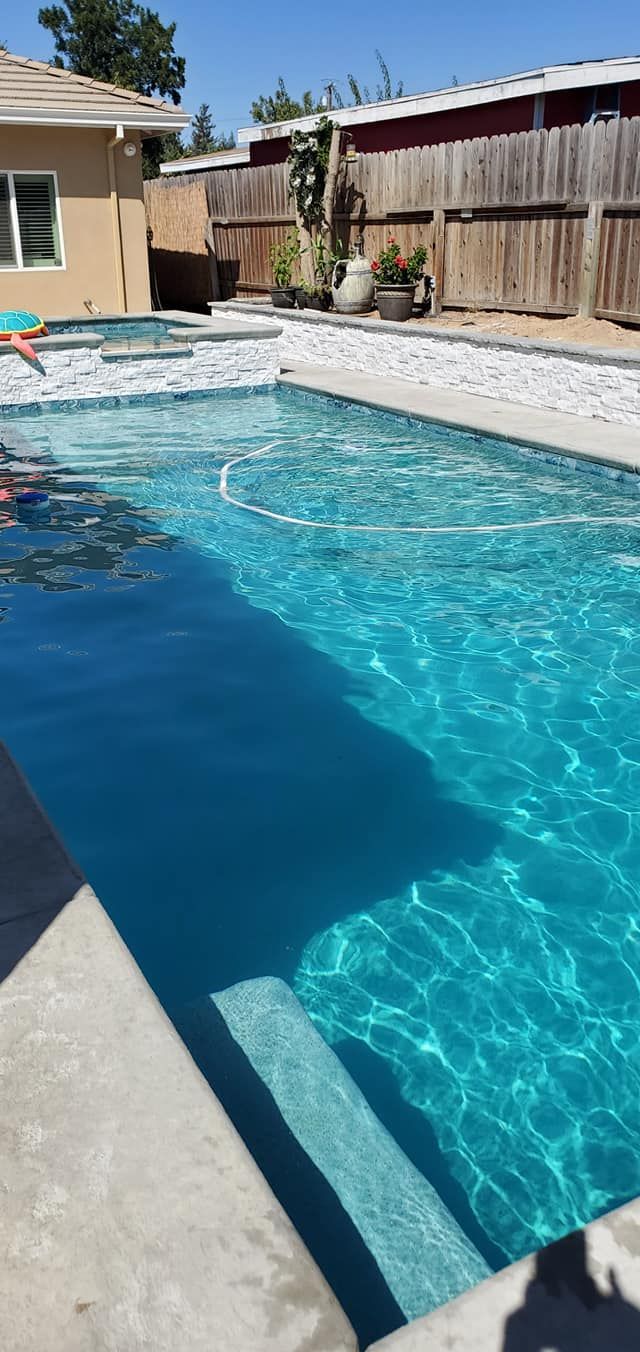 A backyard features a blue swimming pool with a partially covered top, a stone deck, lounge chairs, and a gazebo.