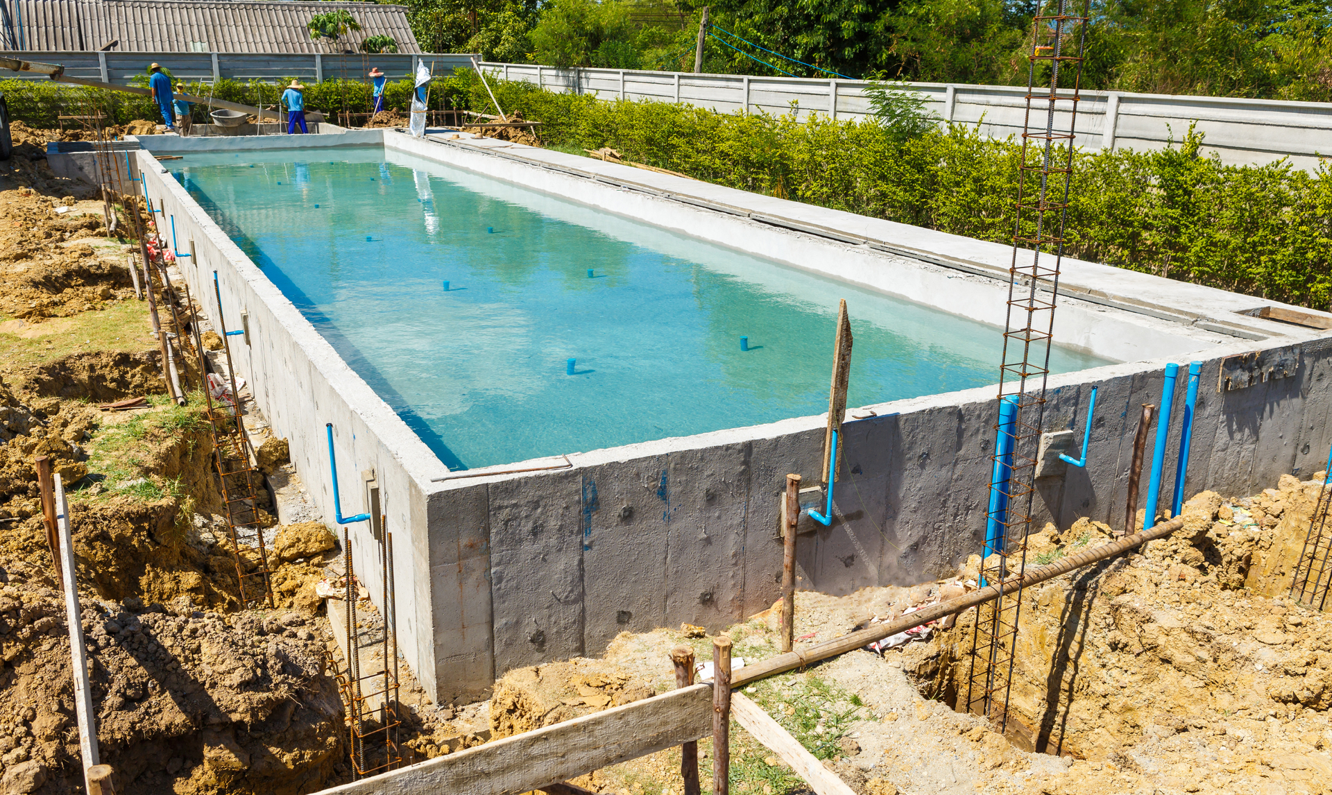 A backyard features a blue swimming pool with a partially covered top, a stone deck, lounge chairs, and a gazebo.