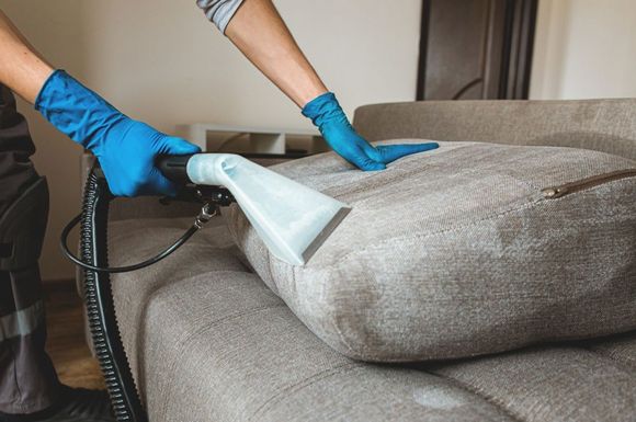 A person is cleaning a couch with a vacuum cleaner