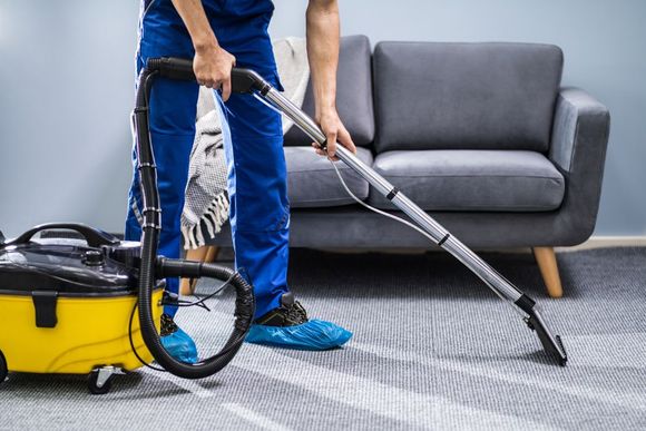 A man is using a vacuum cleaner to clean a white carpet in a living room