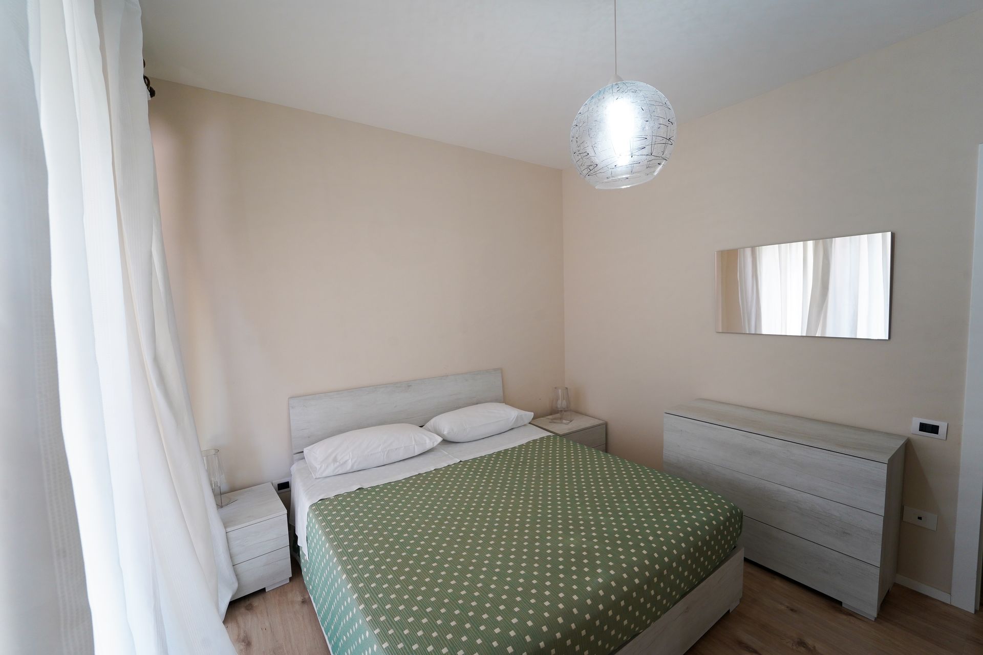 A bedroom with bed, chest of drawers, bedside table and mirror.