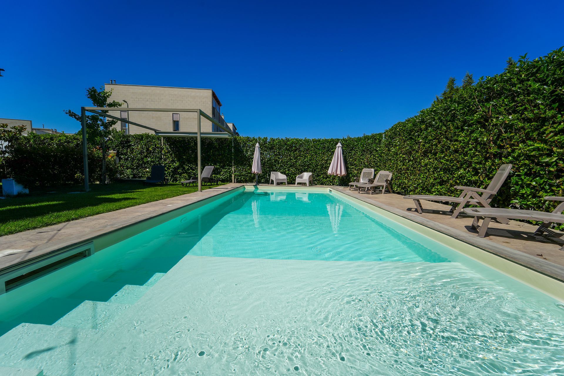 A large swimming pool surrounded by chairs and parasols in a courtyard.