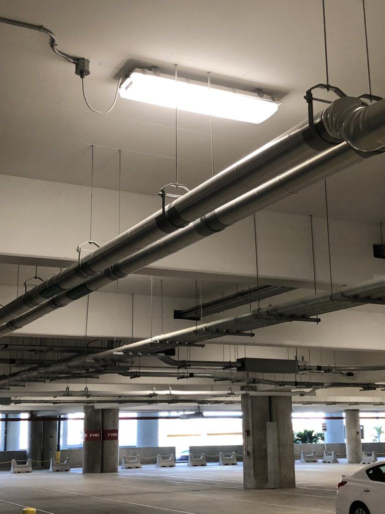 A car is parked in a parking garage with pipes hanging from the ceiling.