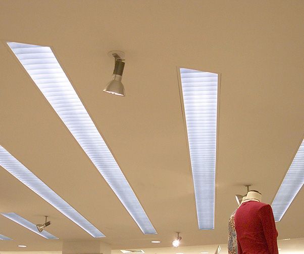 A mannequin in a red jacket is standing under a ceiling with a lot of lights
