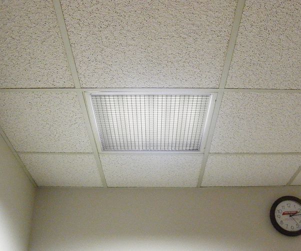 A clock on a wall next to a tiled ceiling