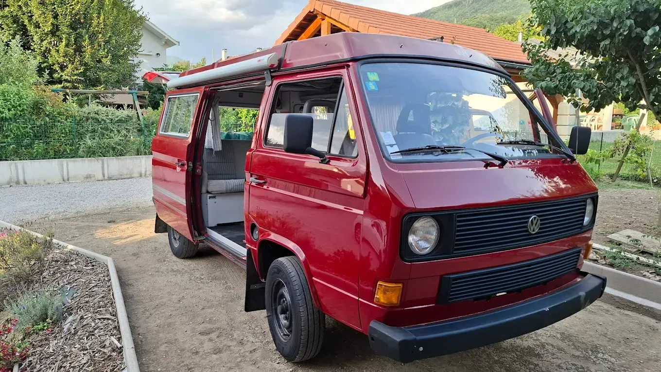Fourgonnette Volkswagen rouge, porte ouverte, garée à l'extérieur.