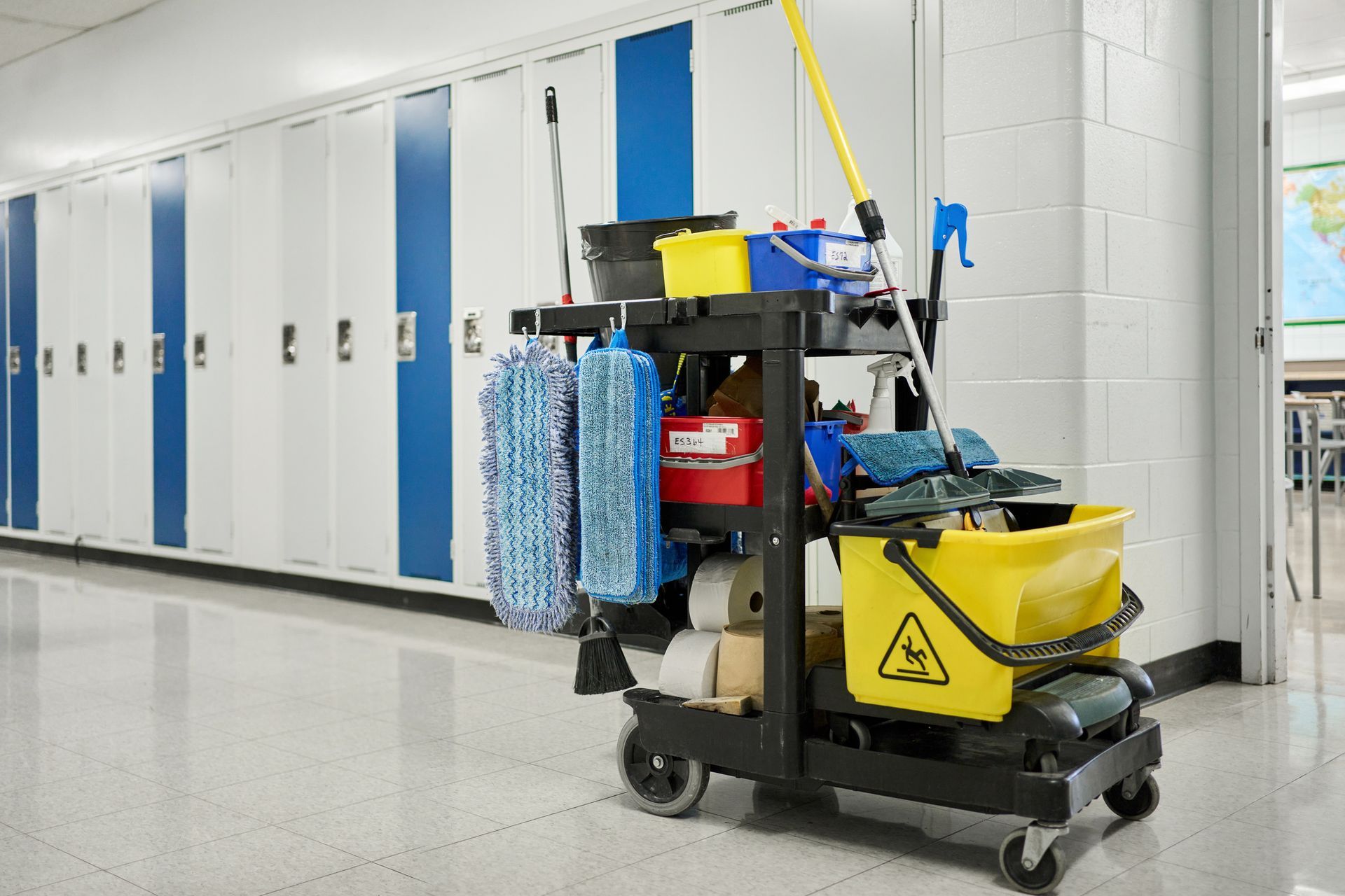 Janitor's cart with cleaning supplies in a school hallway with lockers.
