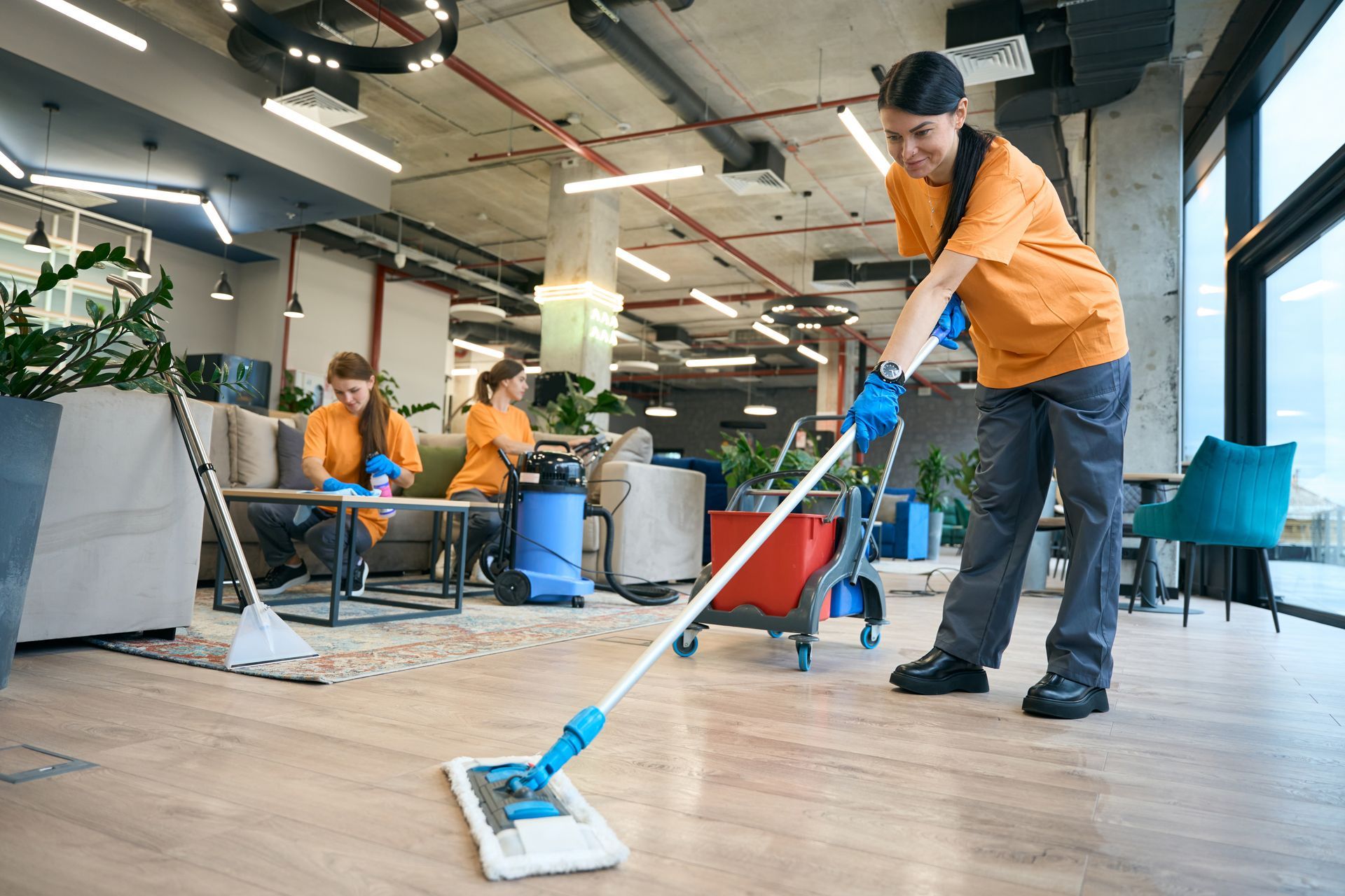 Janitorial service team in uniform vacuuming and cleaning modern office with professional care.