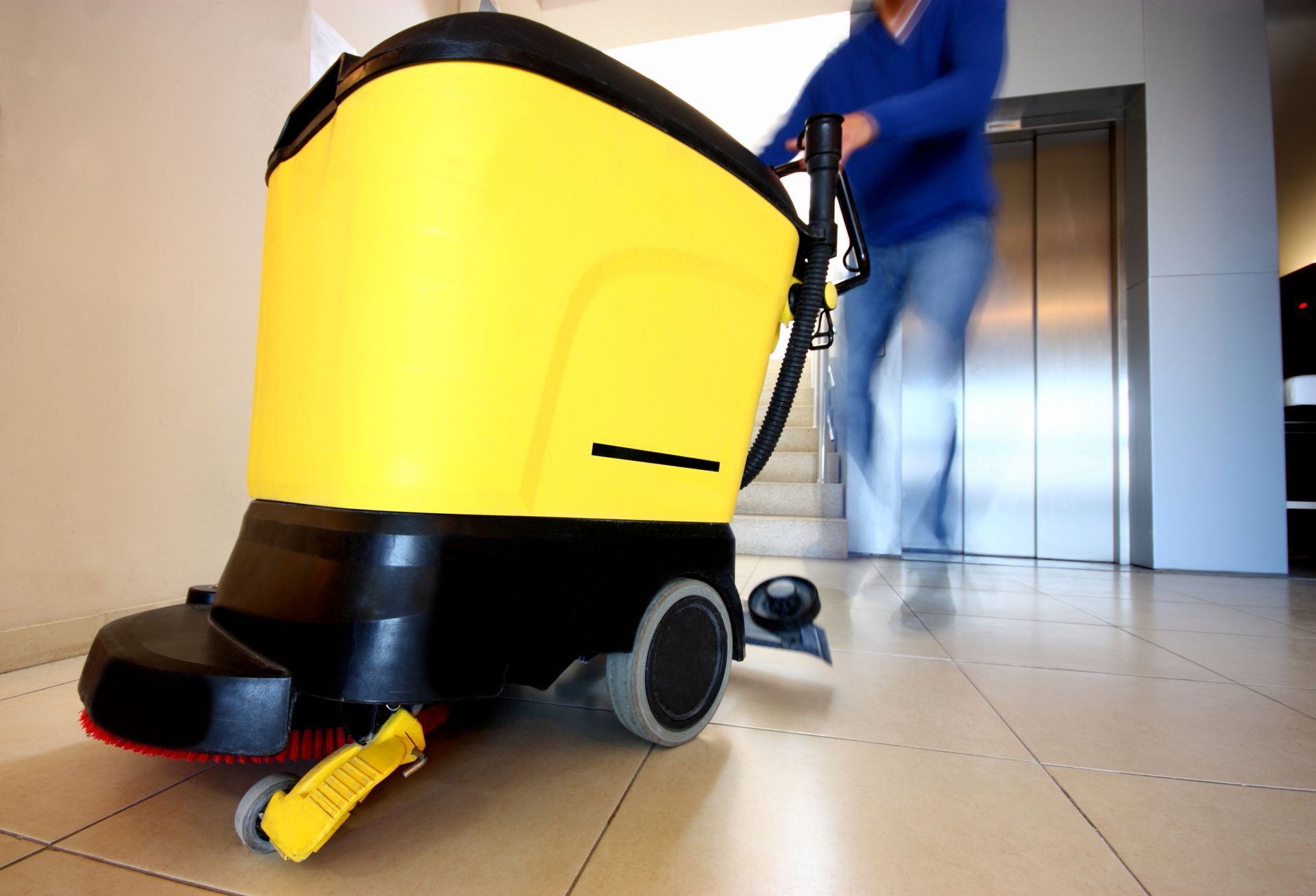Close-up of yellow buffing machine in a hallway, with blurry person, showcasing custodial services.