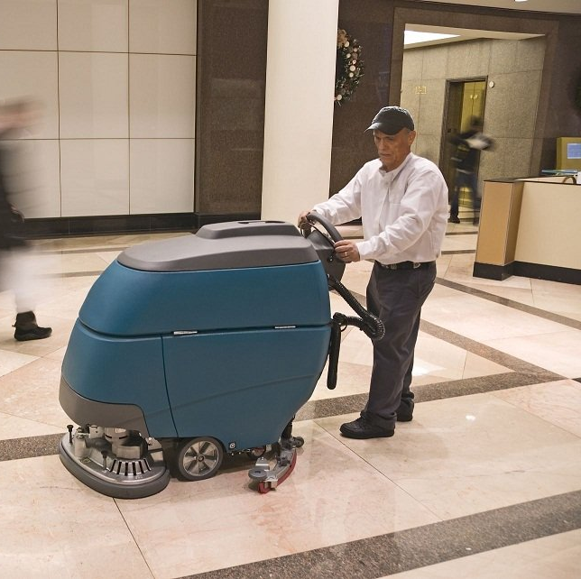 Male janitor cleaning a floor with commercial equipment, showcasing excellent janitorial services.