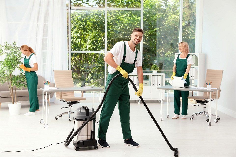 Crew of janitors, two women and a man, with green uniforms, cleaning a white office interior