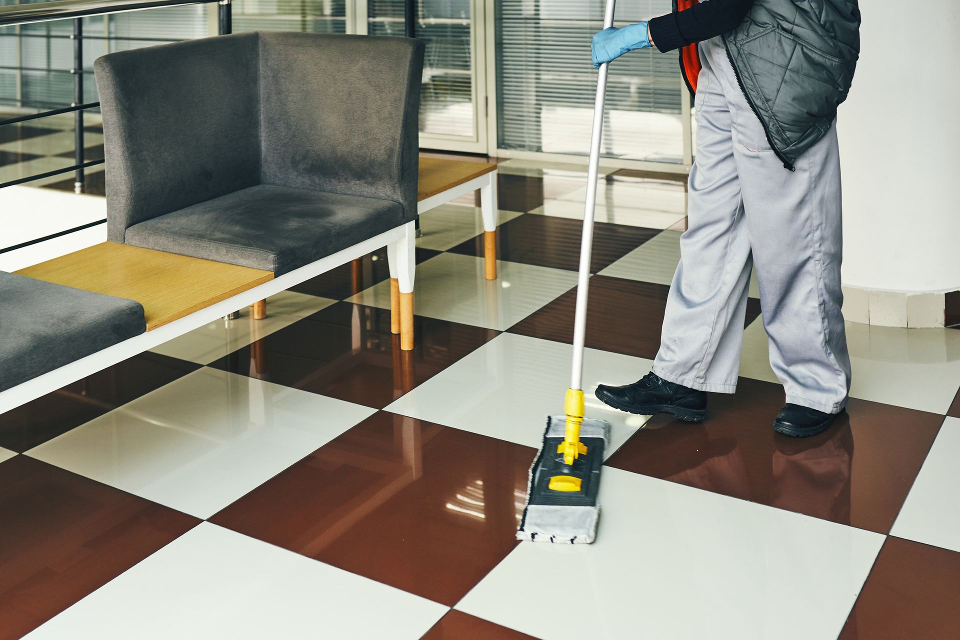 Person mopping checkered floor in clean room with chairs and glass walls.