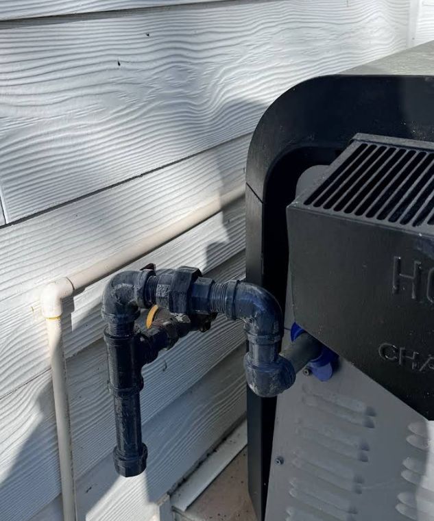 A hose is attached to a heater on the side of a house.