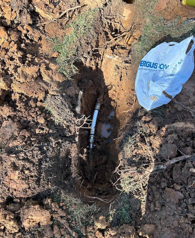 A white bag with the word ergus on it is laying in the dirt next to a pipe.