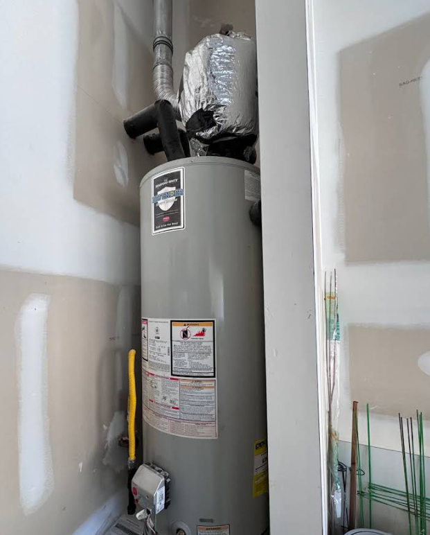 A water heater is sitting in a corner of a room.