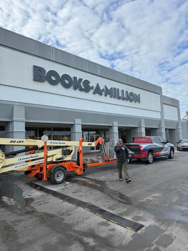 A person walks in front of a Books-A-Million store while towing a construction lift with a truck in the parking lot.