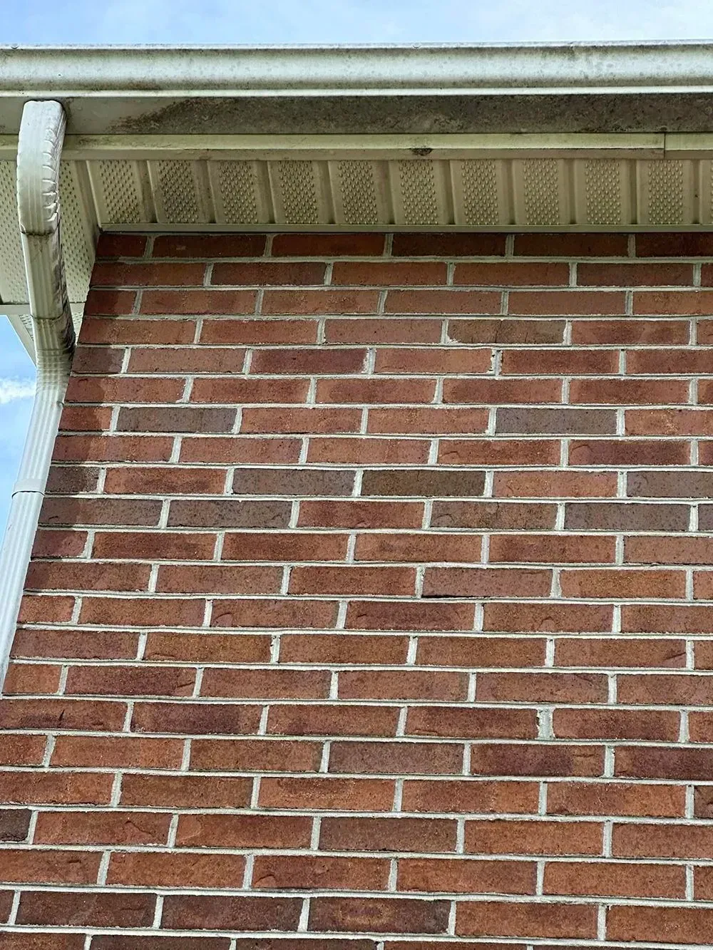 A red brick wall meeting a white roof overhang and gutter corner against a clear blue sky.