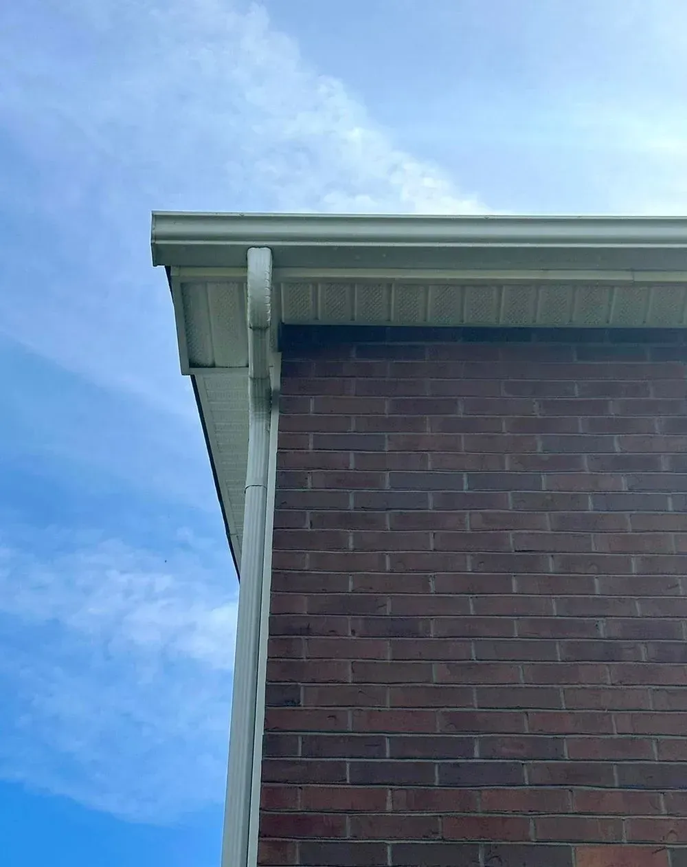 An off-white gutter and corner trim on a brick house under a blue, cloudy sky.
