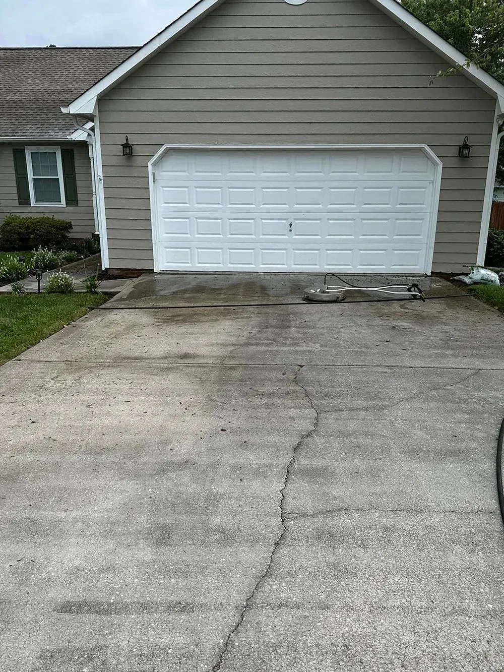 A light-colored house with a single-car garage and a worn concrete driveway featuring a large crack.