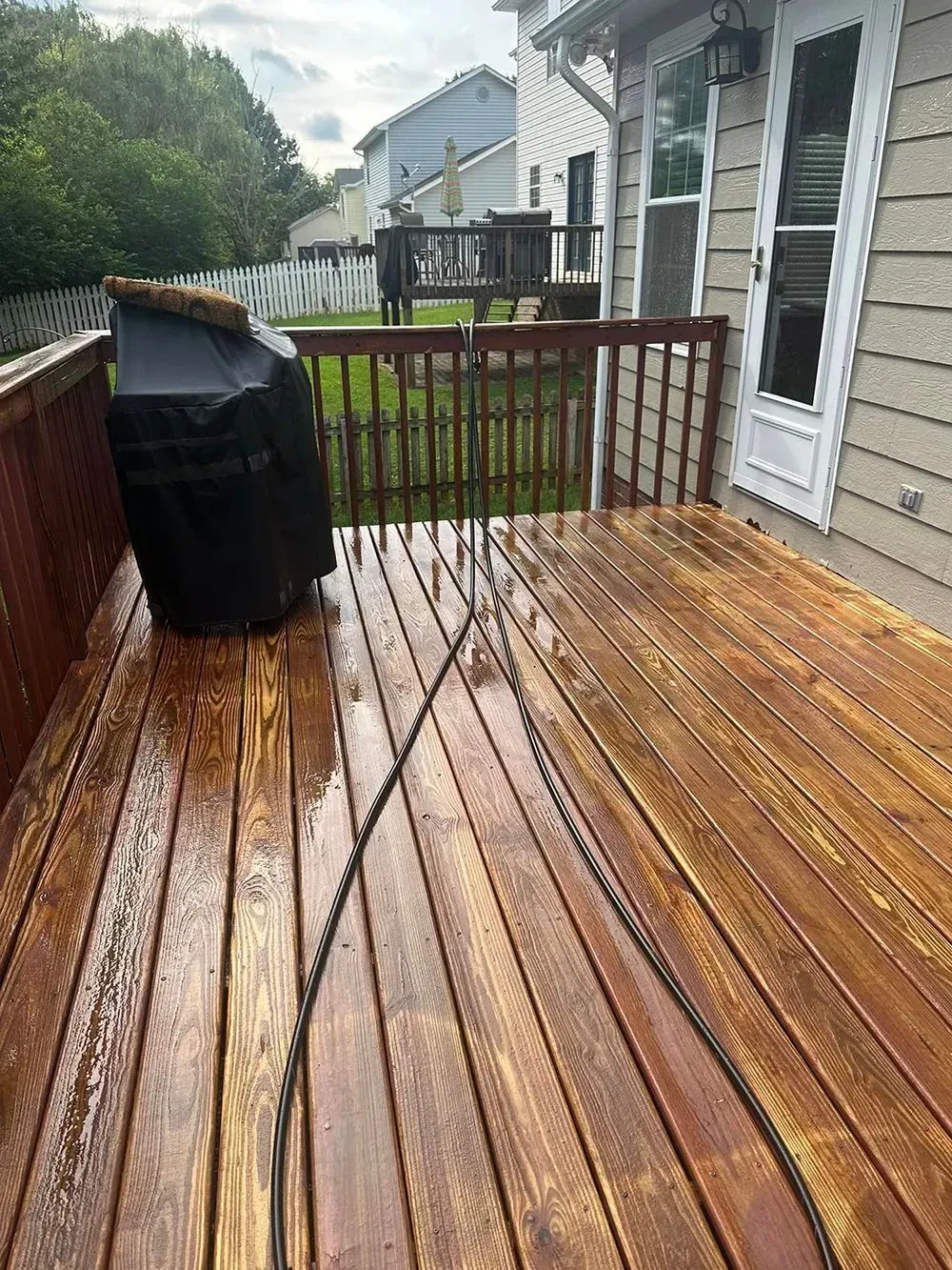 A black grill sits on a wet wooden deck next to a railing, with a thin rope stretching across the foreground.