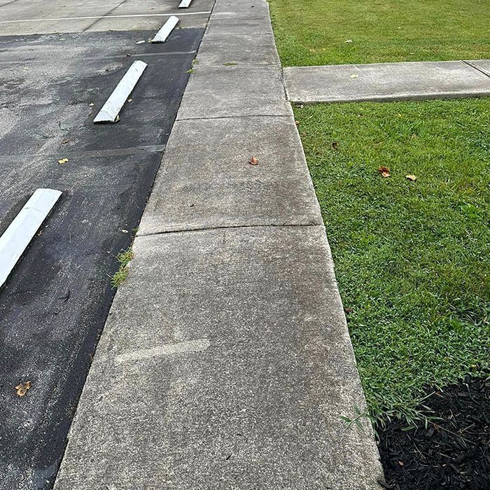 A concrete sidewalk runs between a paved parking lot with white wheel stops and a grassy lawn.