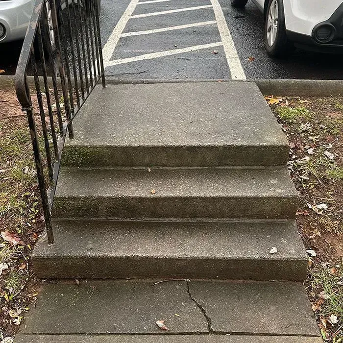 A set of three concrete steps leading up to a sidewalk, flanked by a black metal railing.