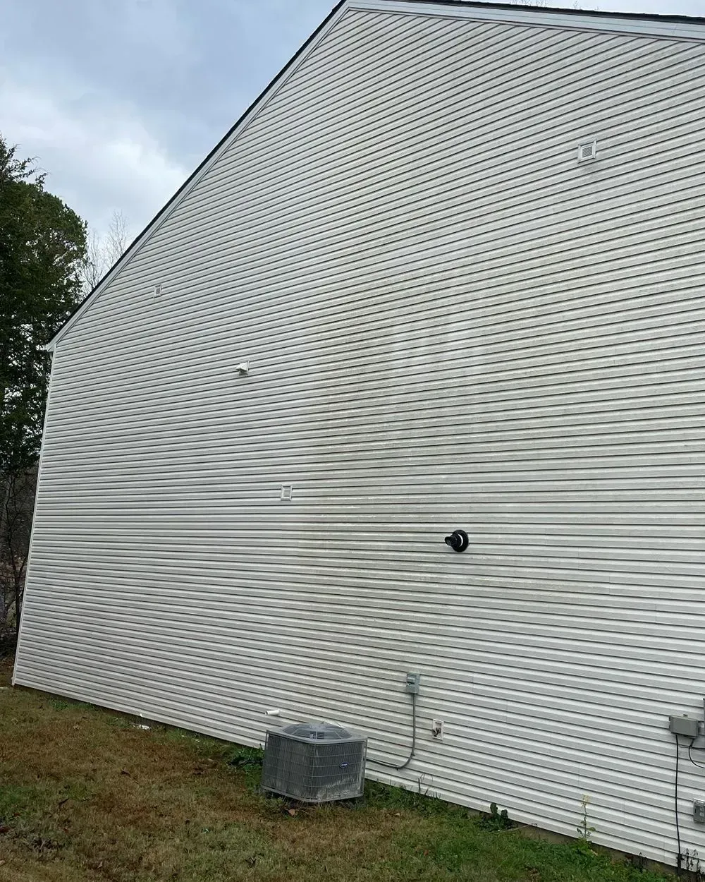 The side of a house with white horizontal vinyl siding, a small outdoor AC unit, and a black circular light fixture.