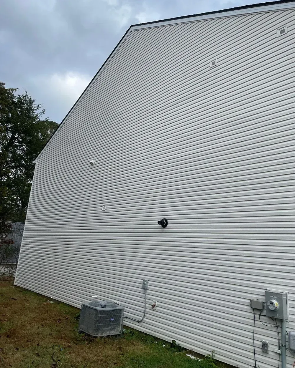 A side view of a house with white horizontal vinyl siding, a gray A/C unit, and an electrical box on a grassy lot.