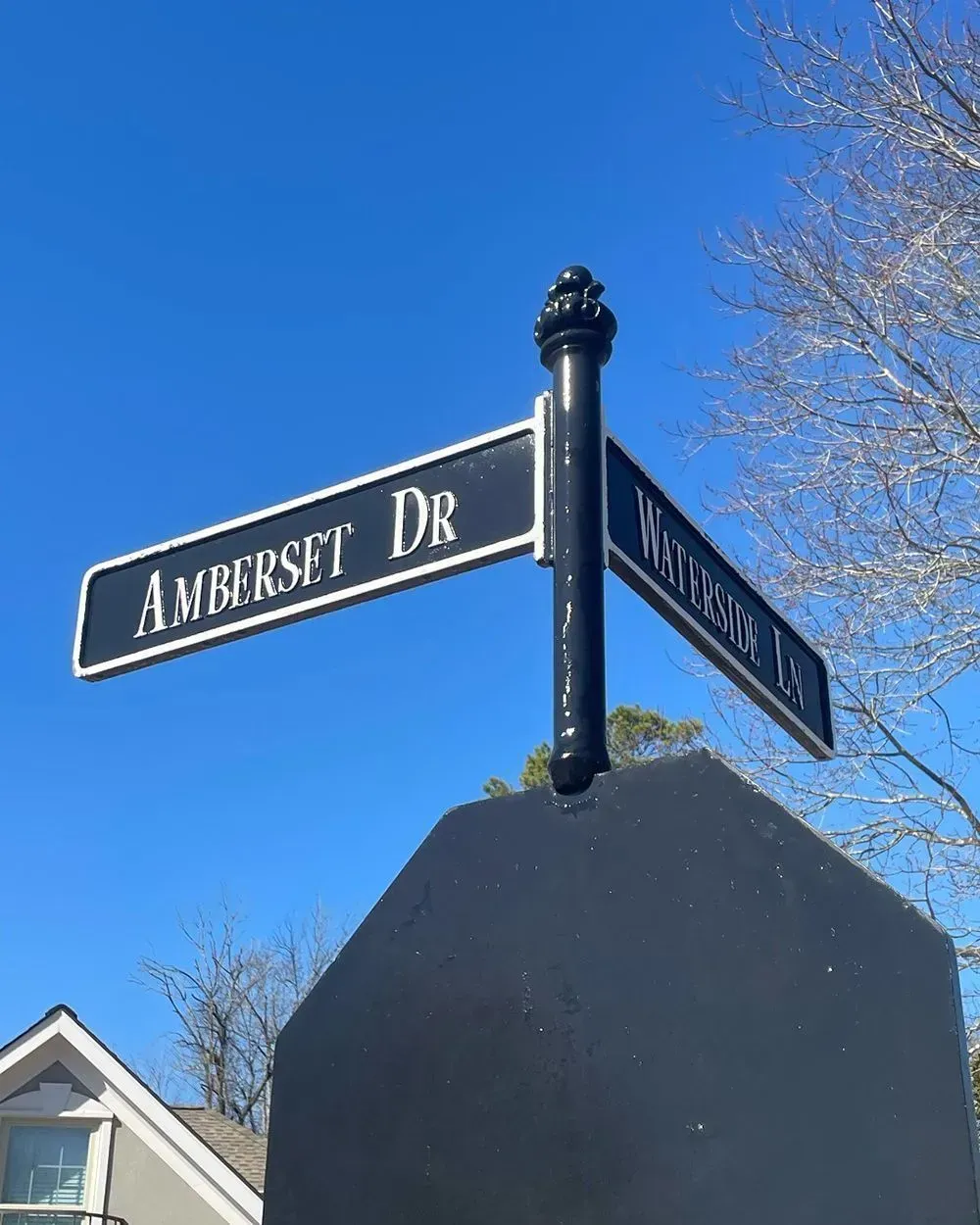 Black street sign post for Amberset Dr and a cross street against a bright blue sky.