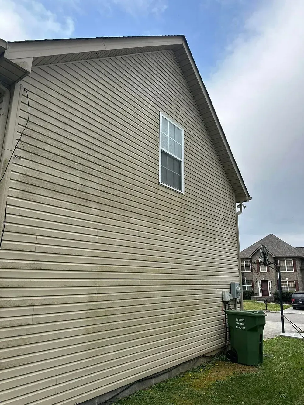 A side view of a house exterior with stained, light-colored horizontal vinyl siding and a single window.
