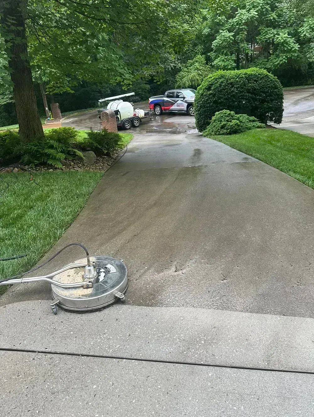 A circular surface cleaner on a concrete driveway, partially cleaned to show the contrast with the dirtier concrete.