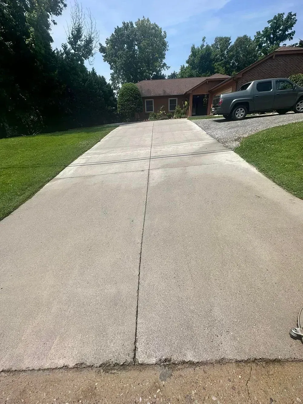 A long, straight concrete driveway leads toward a house with a green lawn and a parked truck in the background.