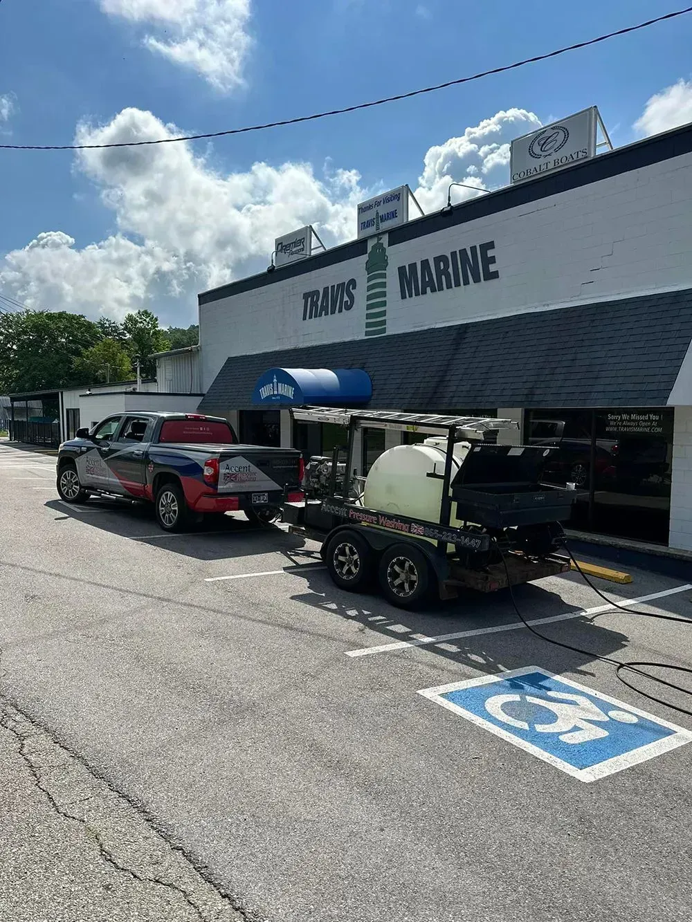 A truck towing a trailer with a white water tank parked in front of a building labeled 