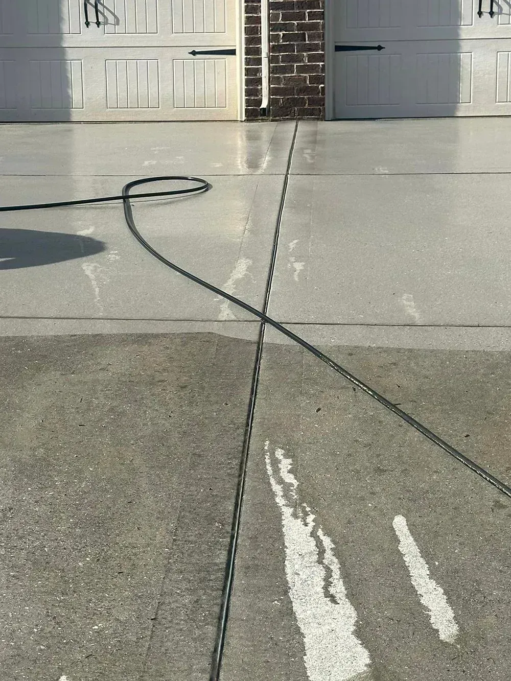 A black power cord snakes across a driveway, spanning across a dark concrete section and a freshly pressure-washed area.