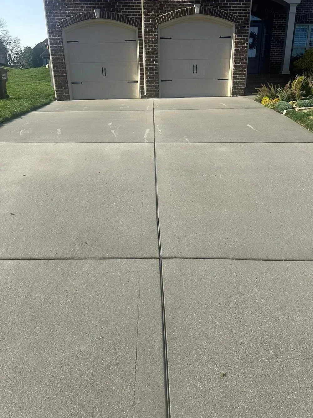 A driveway with two concrete lanes leading to a brick house with two closed garage doors.